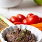 A small white dish filled with a bean spread and fresh veggies surrounding the small dish.
