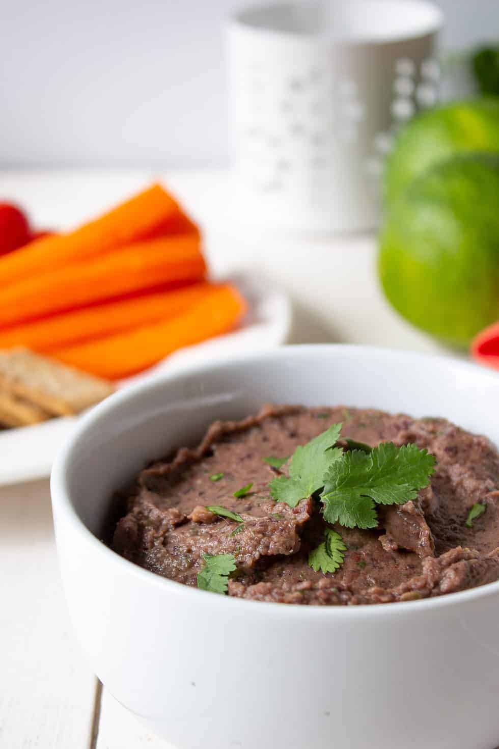 Black dip topped with fresh cilantro with fresh cut veggies behind the dip. 