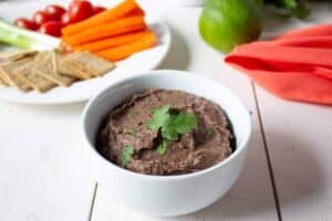A white bowl filled with a dark bean dip topped with fresh cilantro.