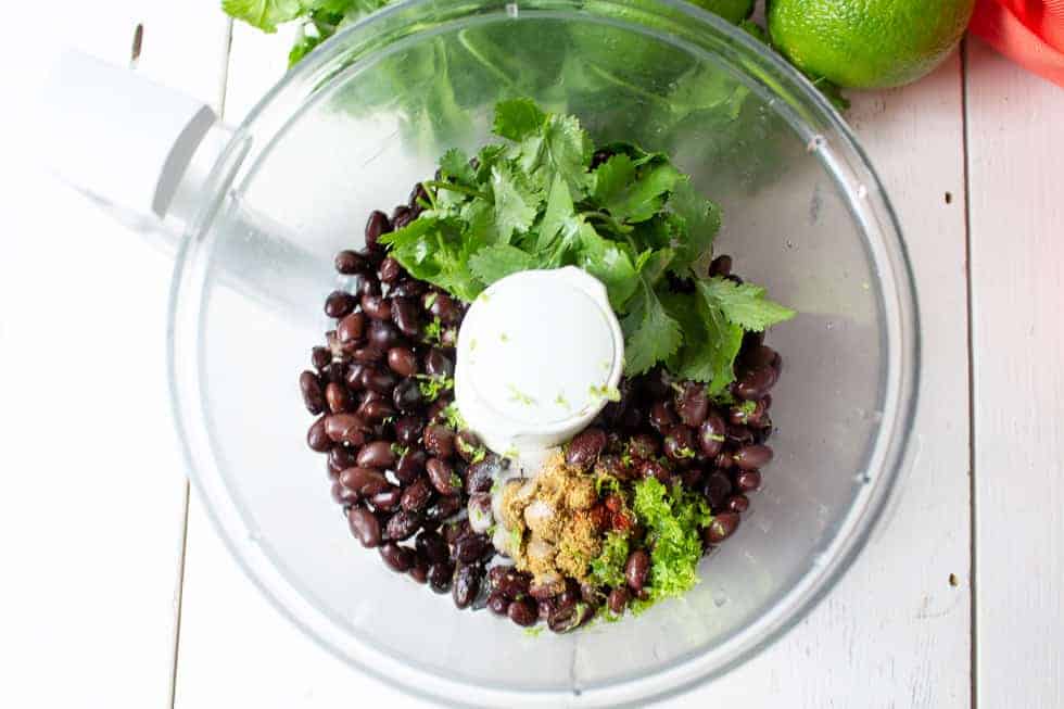 A food processor bowl filled with black beans, seasonings, and fresh cilantro.