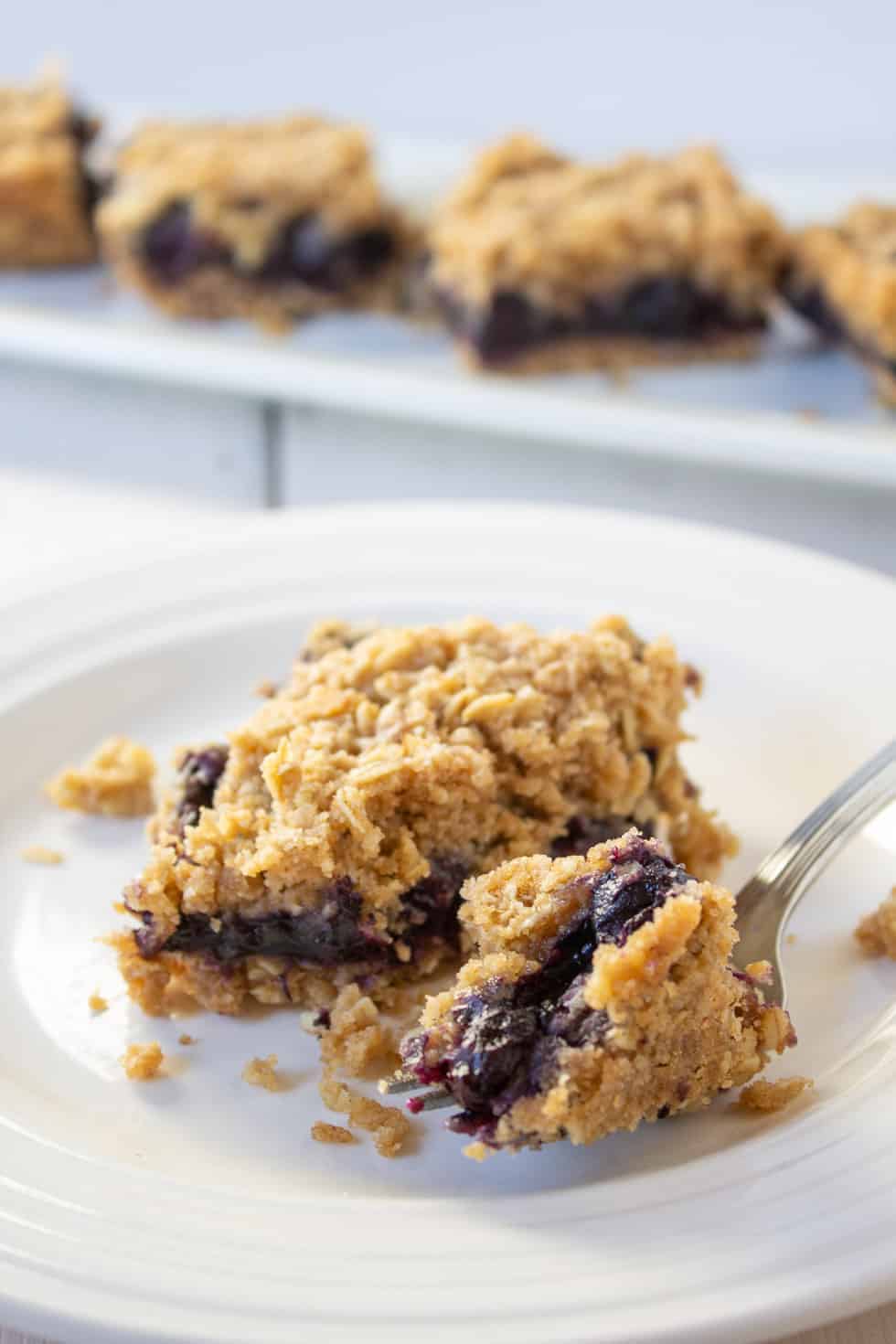 A blueberry dessert on a plate with a small piece of dessert cut onto a fork. 