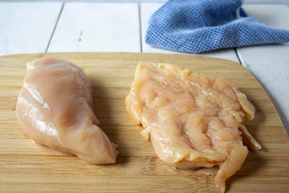 Two chicken breasts on a wooden cutting board.