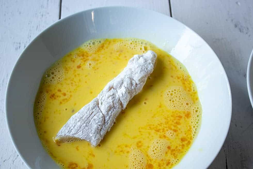 Chicken breast in a bowl filled with mixed eggs.