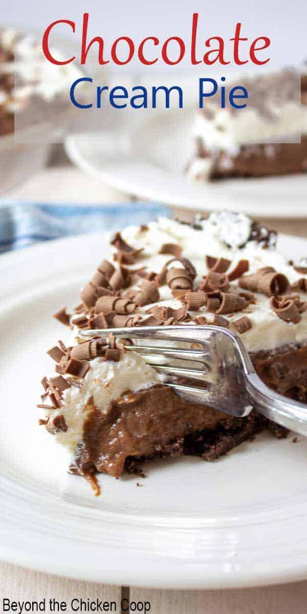 A fork slicing into a pie of chocolate pie topped with whipped cream.