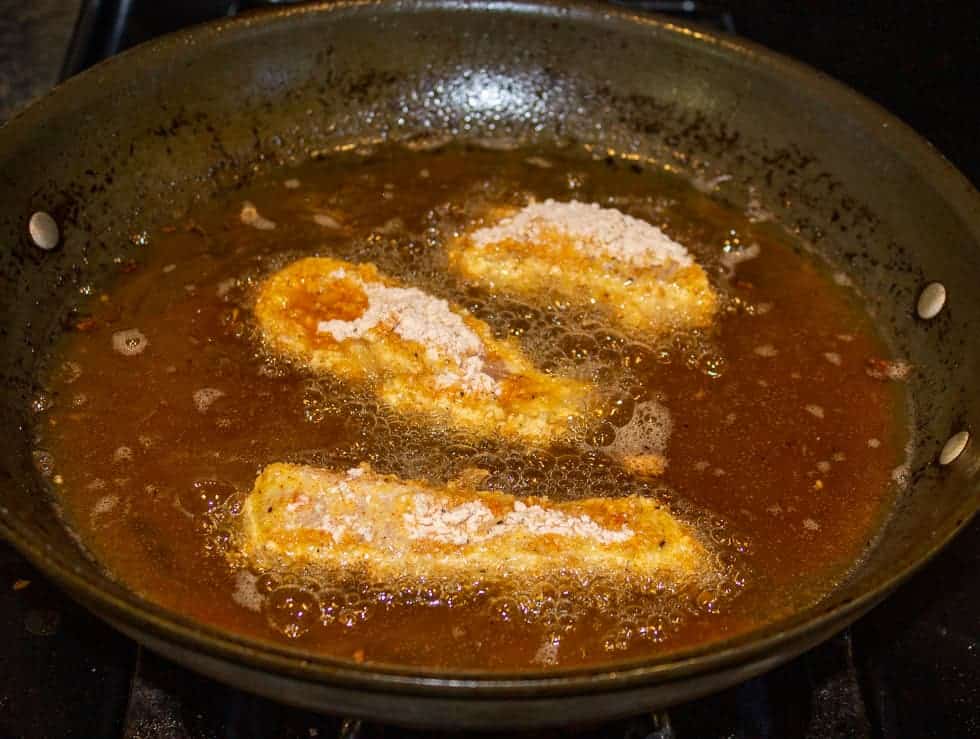 Chicken frying in a shallow pan with oil.