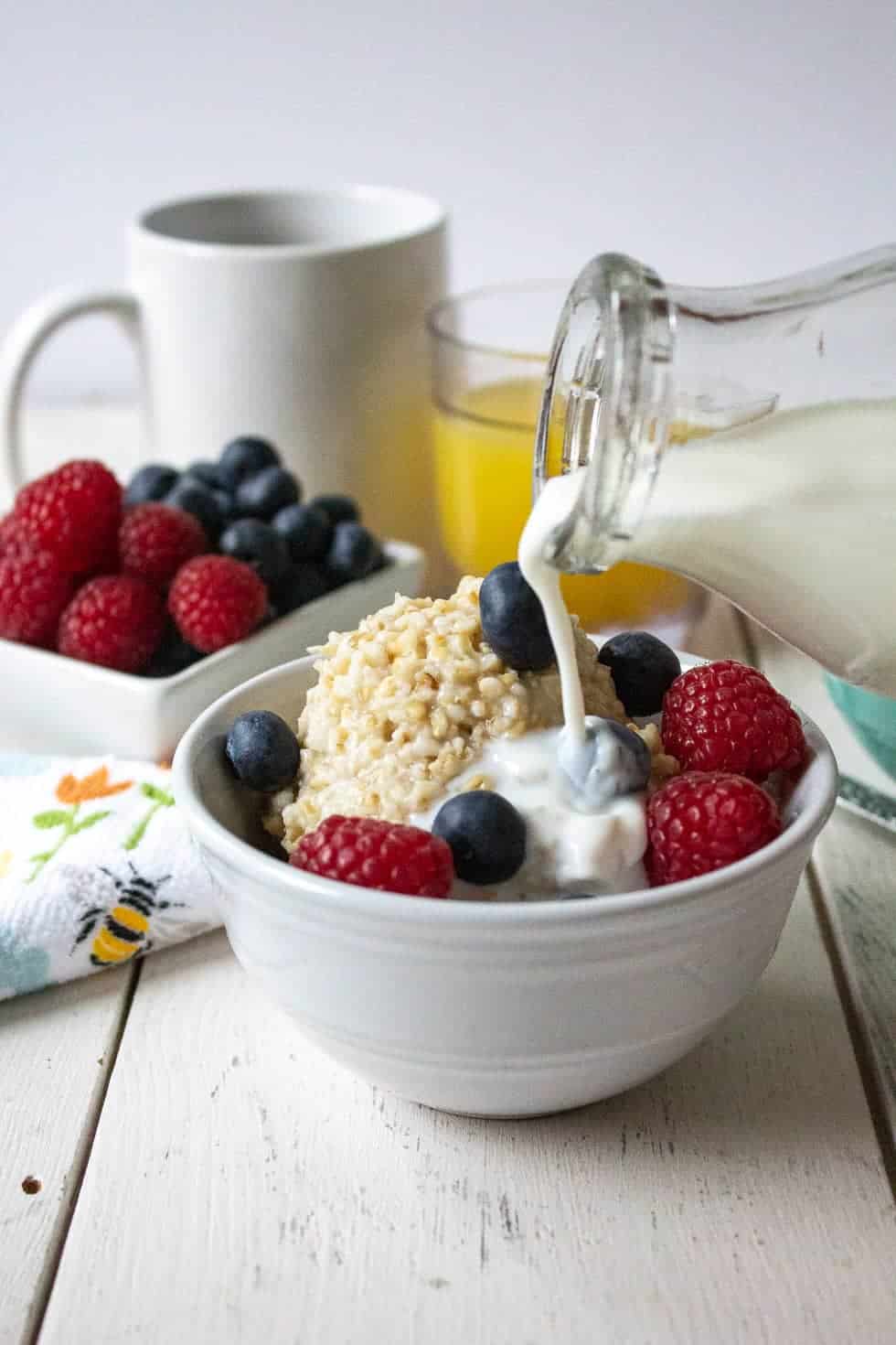 Milk being poured over a bowl full of oatmeal and fruit. 