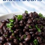 A large bowl filled with cooked black beans topped with a fresh green herb.