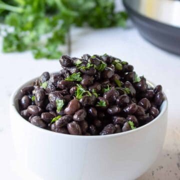 A white bowl filled with cooked black beans topped with a fresh green herb.