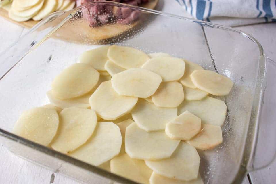 Sliced potatoes layered in a glass casserole dish.