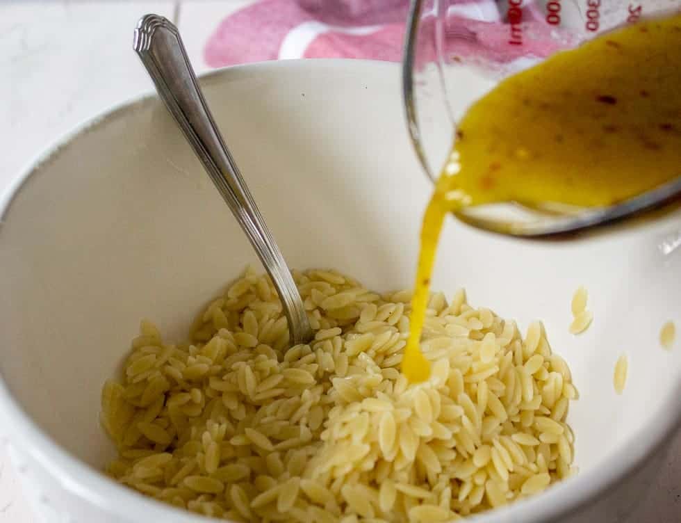Pouring a dressing over orzo pasta.