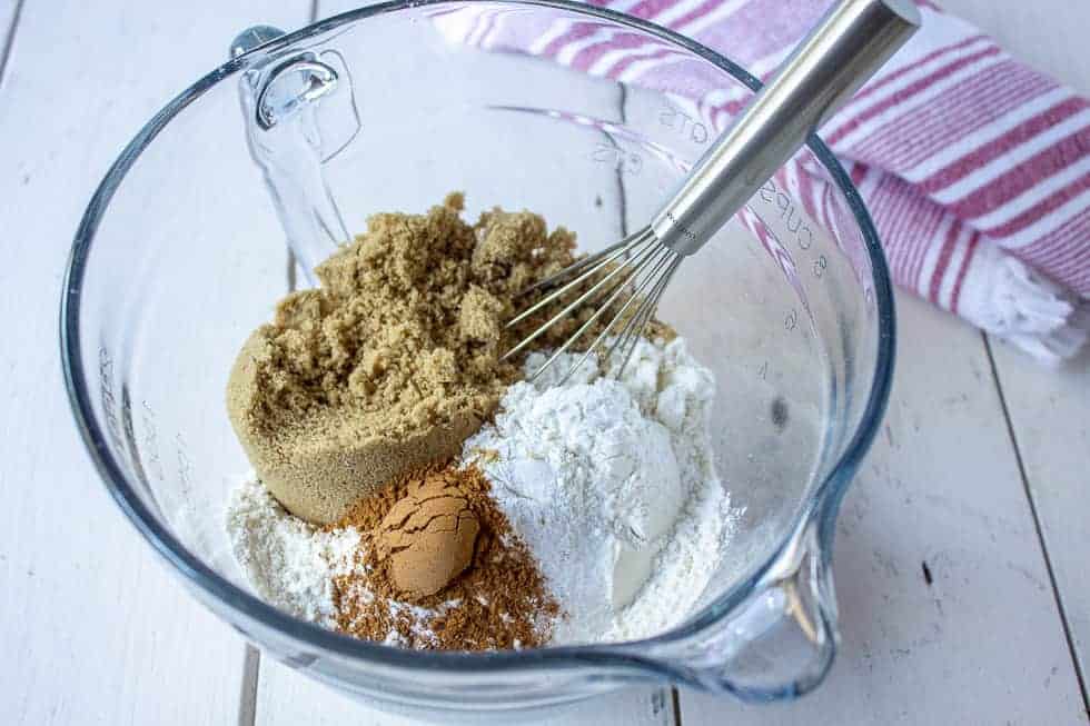 A bowl with flour, cinnamon and brown sugar with a wire whisk in the bowl.