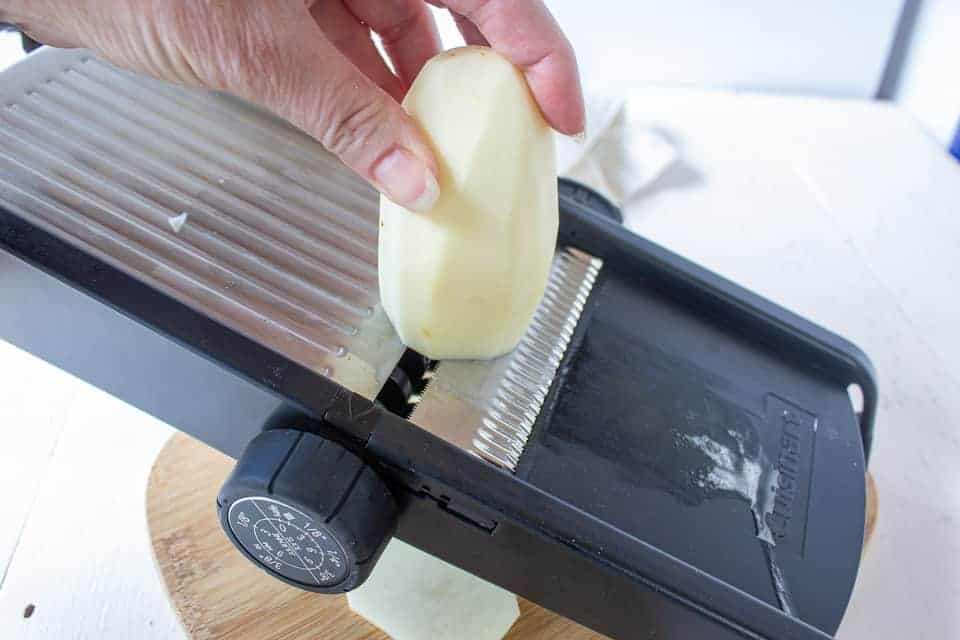 A potato being sliced on a mandoline.