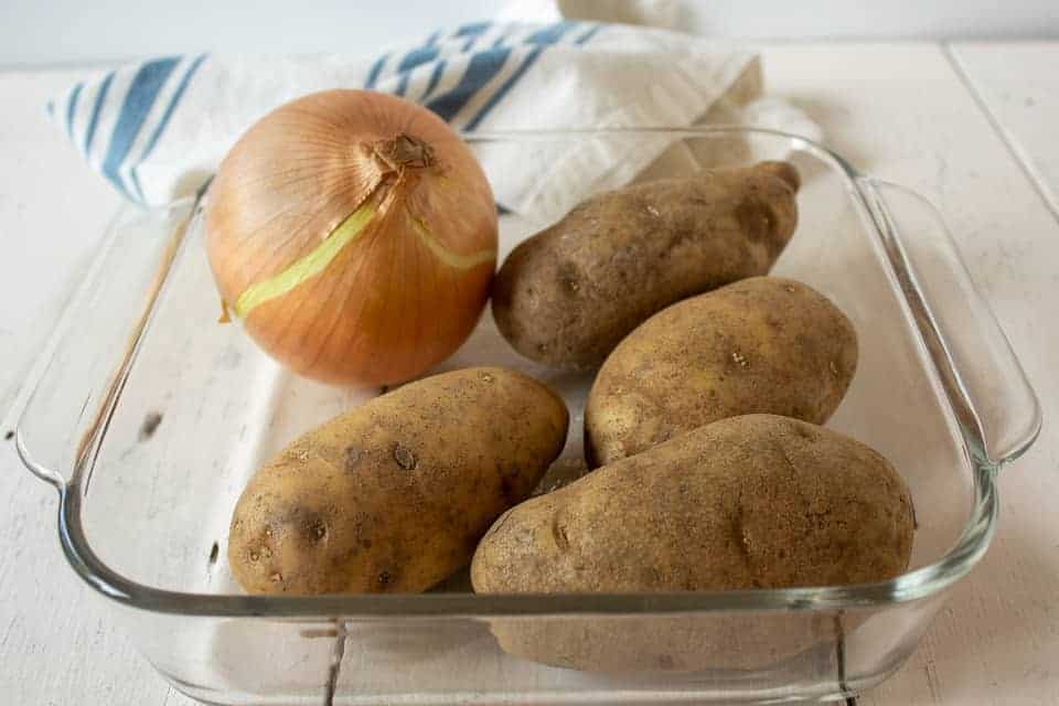 Potatoes and an onion sitting in a glass casserole dish.