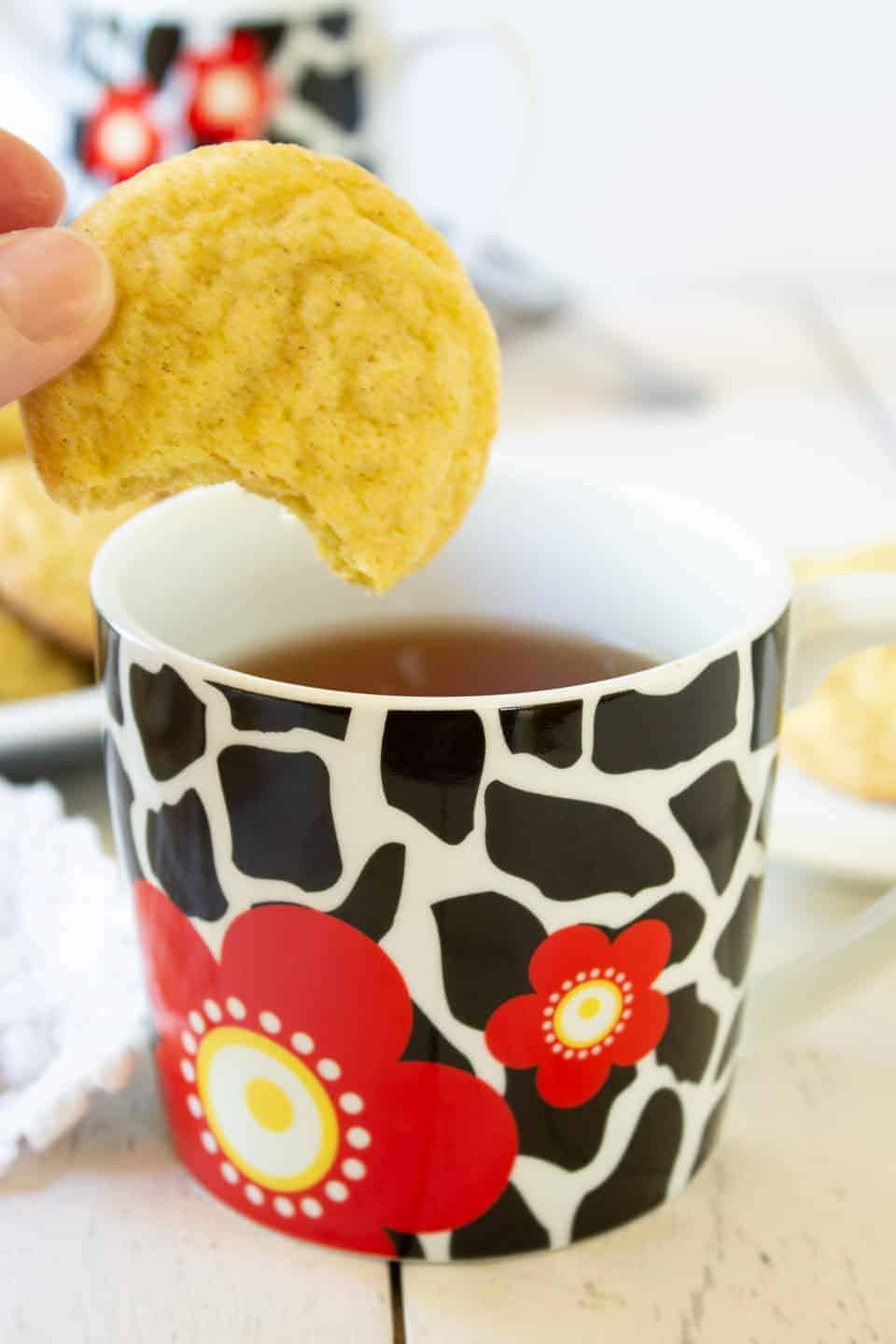 A cookie with a bite out of it being dipped into a cup of tea. 