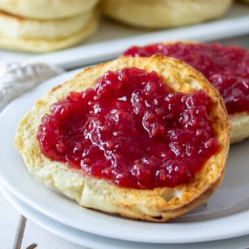 A toasted muffin with red raspberry jam spread on the muffin.