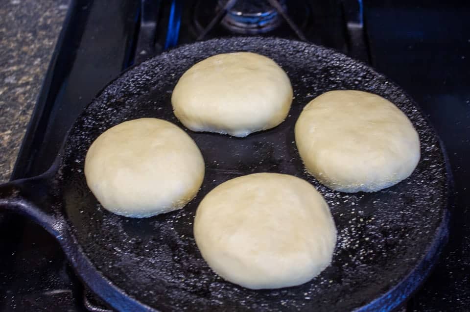 English muffins cooking on a cast iron skillet.