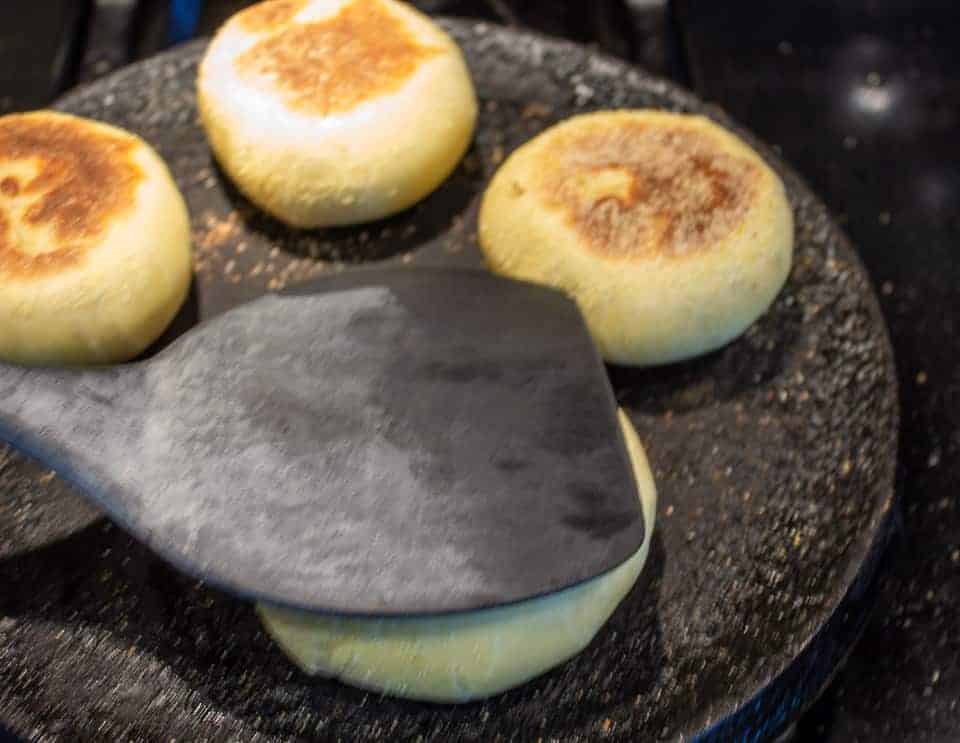 Pressing down an English muffin with a black spatula.