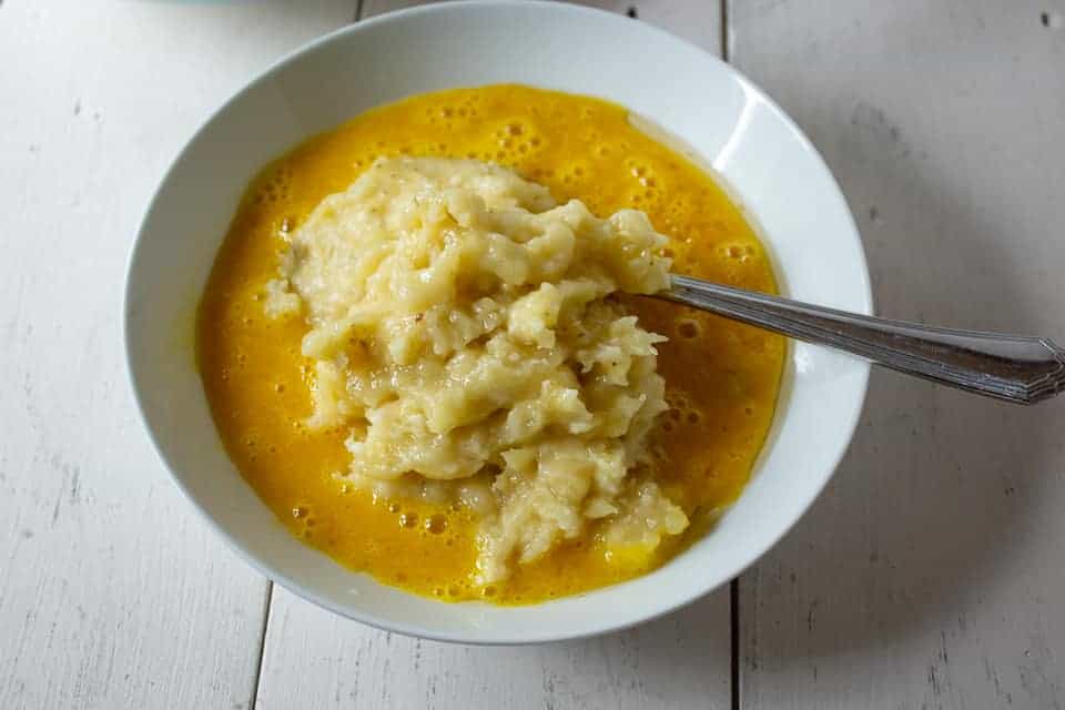 An egg mixture topped with mashed bananas and a fork.