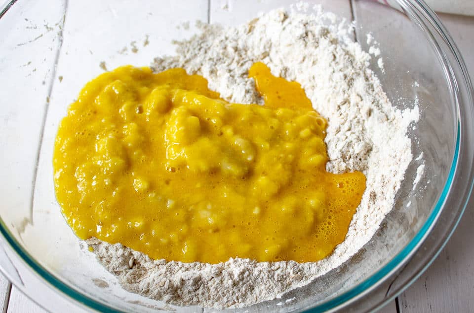 A flour and oat mixture with added eggs and bananas in a large glass bowl.