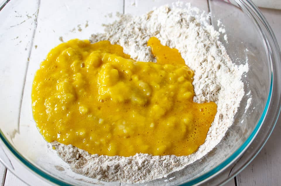 A flour and oat mixture with added eggs and bananas in a large glass bowl.