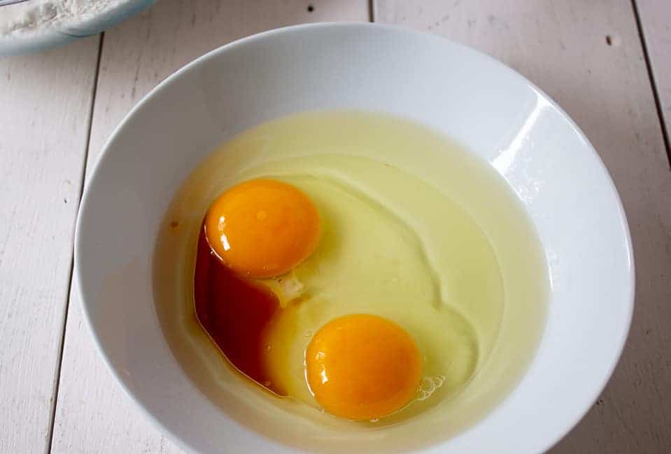 A small white bowl with two eggs, vanilla and oil.