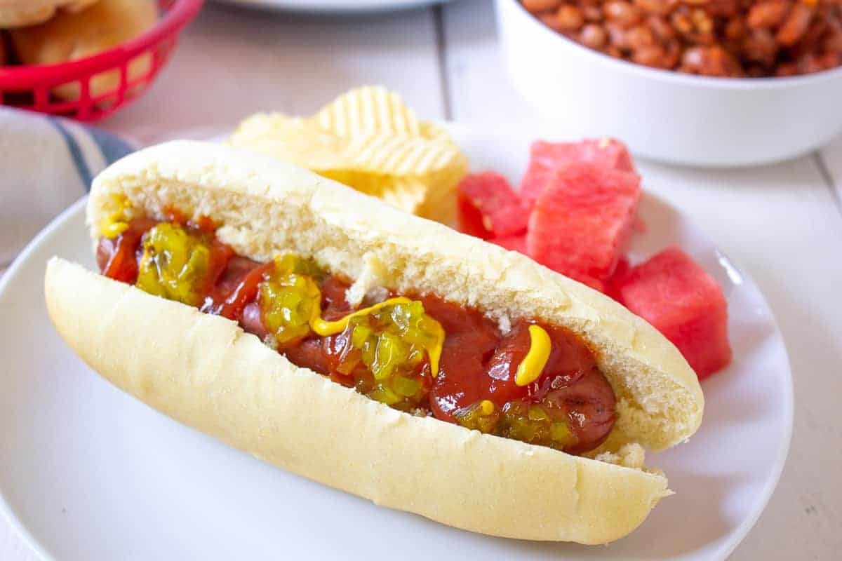 A hot dog topped with ketchup, mustard and relish sitting in a bun.