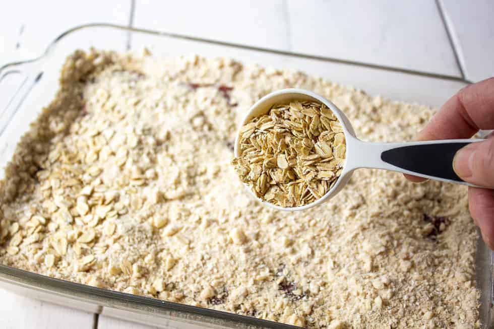 A measuring cup pouring oats on top of a crust.