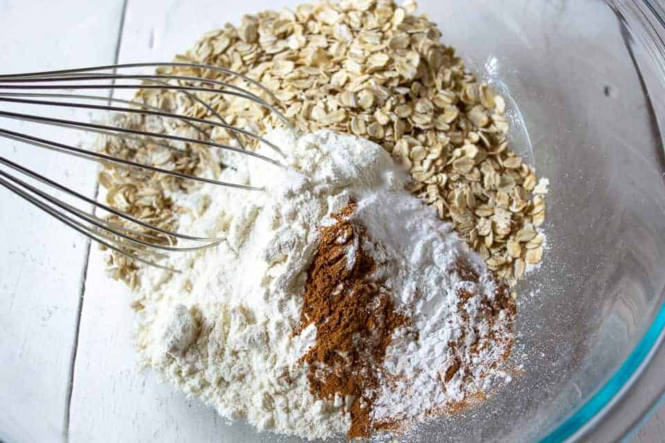 A bowl with a whisk filled with oatmeal, flour, cinnamon and a few other ingredients.