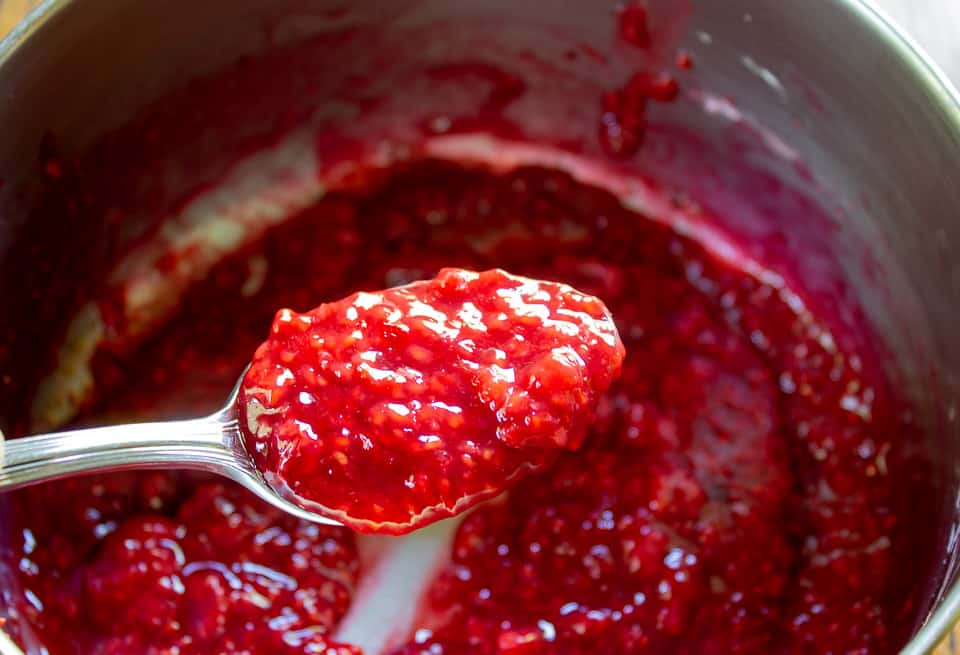 Raspberry filling on a spoon over a pot with raspberry filling.