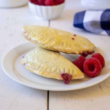 Baked raspberry turnovers on a white plate with fresh raspberries.