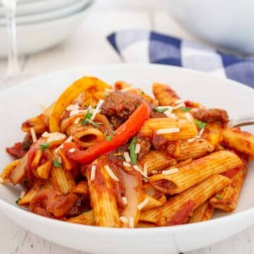 A white bowl filled with pasta with peppers and sausage.