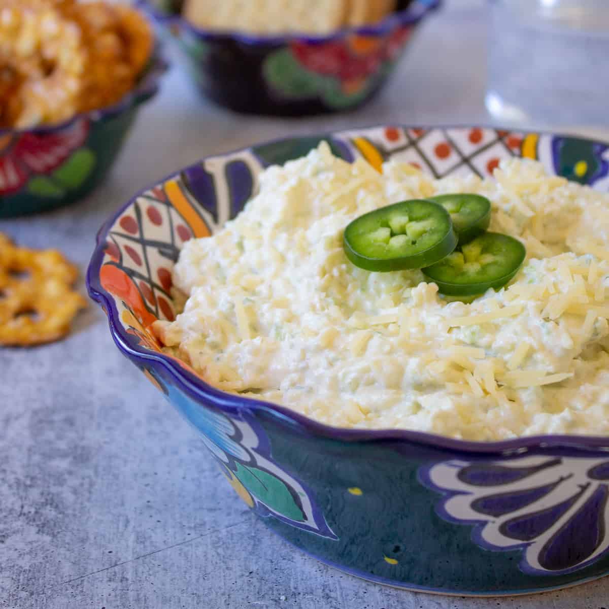 Artichoke dip topped with sliced jalapenos in a colorful bowl.