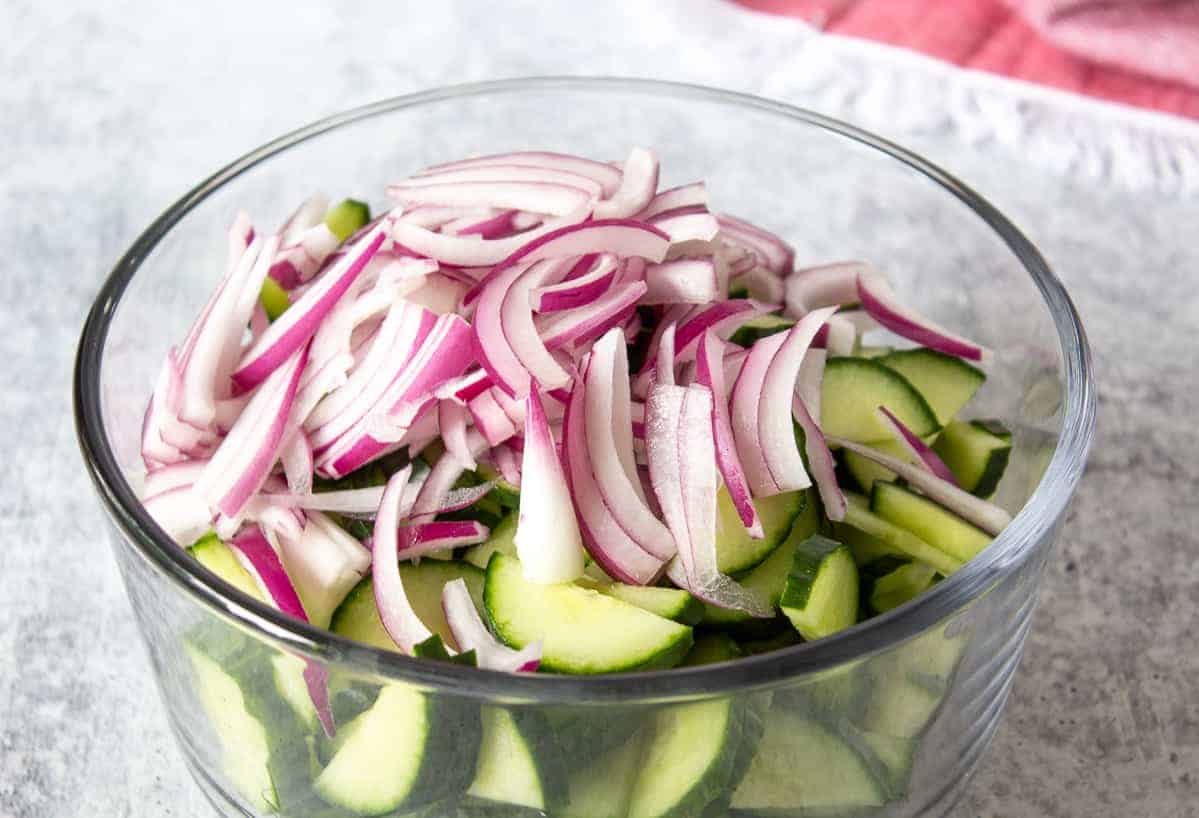 A glass bowl filled with sliced cucumbers and red onions.
