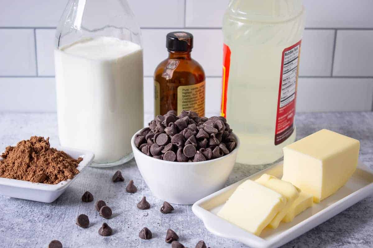 Chocolate chips, butter, cream and cocoa powder displayed on a gray board.