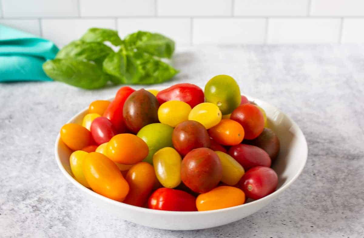 A bowl filled with green, yellow, red and orange cherry tomatoes.