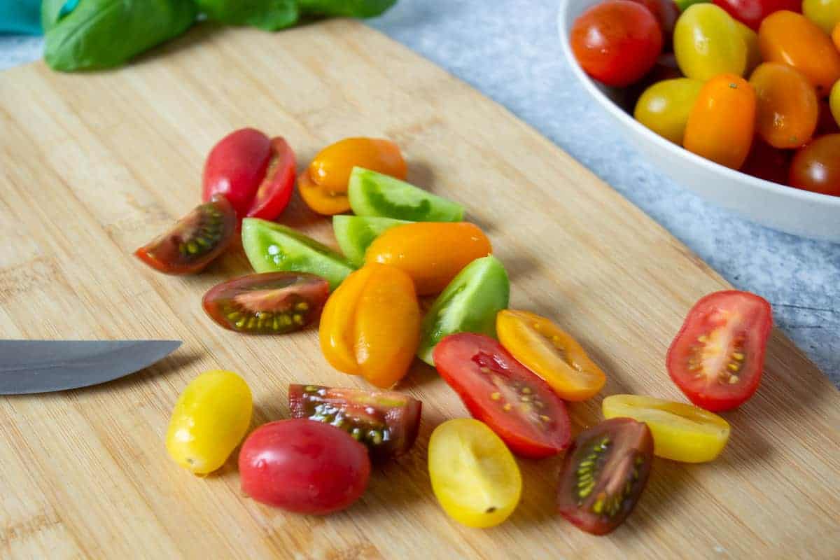 Small colored cherry tomatoes cut in half on a wooden cutting board.