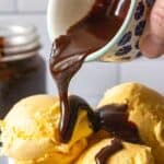 Hot fudge sauce being poured over a bowl of vanilla ice cream.