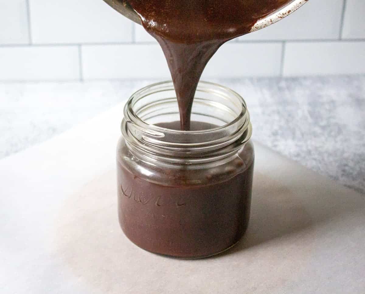 Pouring hot fudge sauce into a jar.