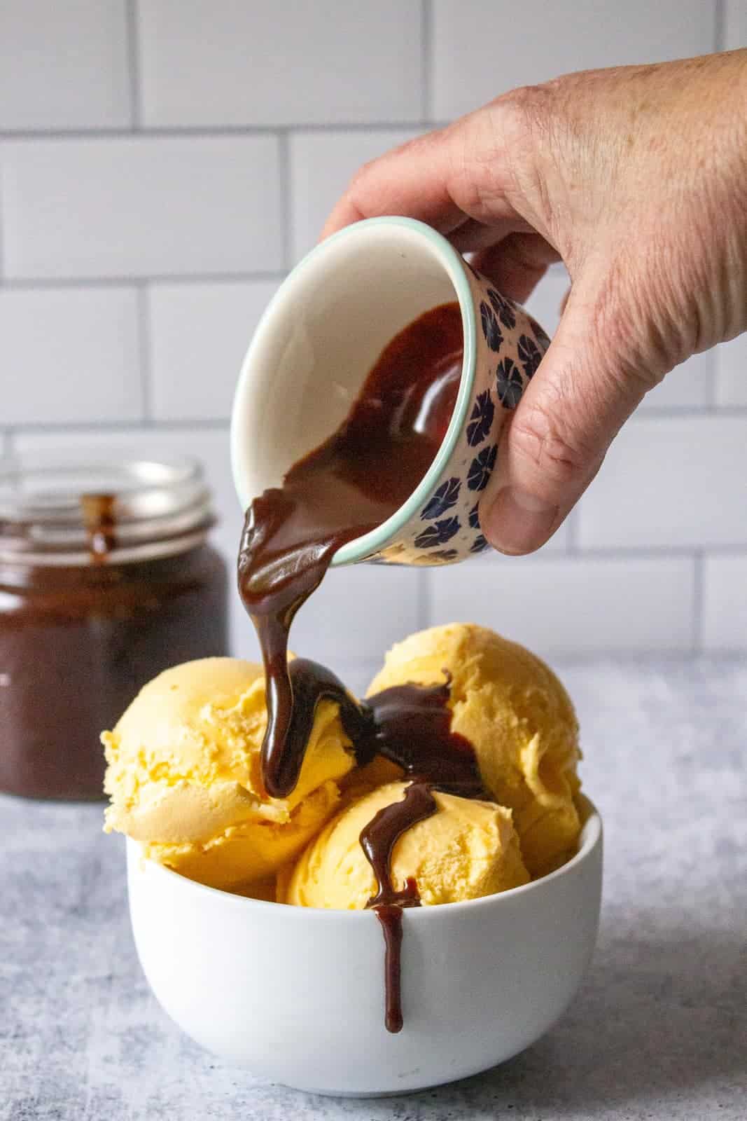 Chocolate sauce being poured over scoops of vanilla ice cream. 