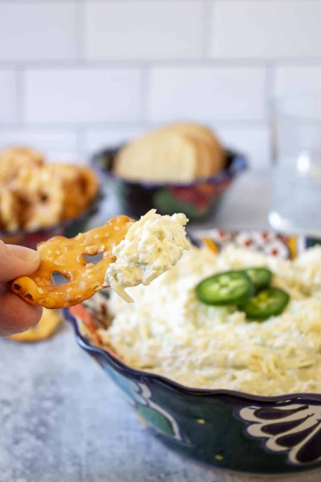 A flat pretzel with a scoop of artichoke dip on top.