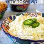 A colorful blue bowl filled with artichoke dip and topped with sliced jalapenos.