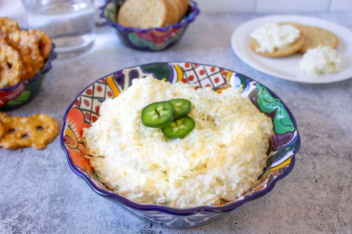 A colorful bowl filled with artichoke dip and topped with sliced jalapenos.