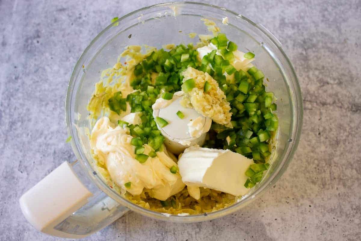 Ingredients for making artichoke dip in a food processor bowl.