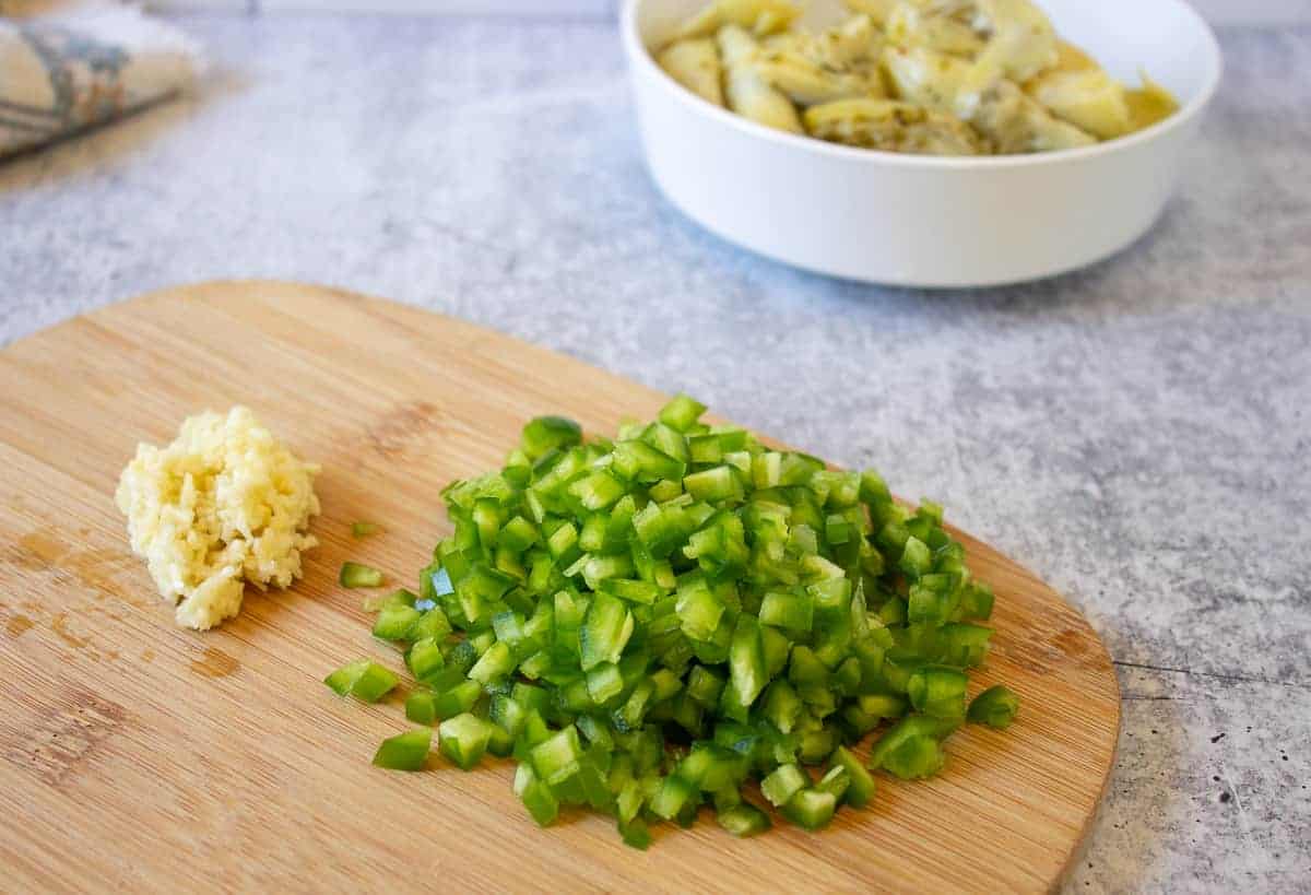 Finely chopped jalapenos and minced garlic on a wooden cutting board.