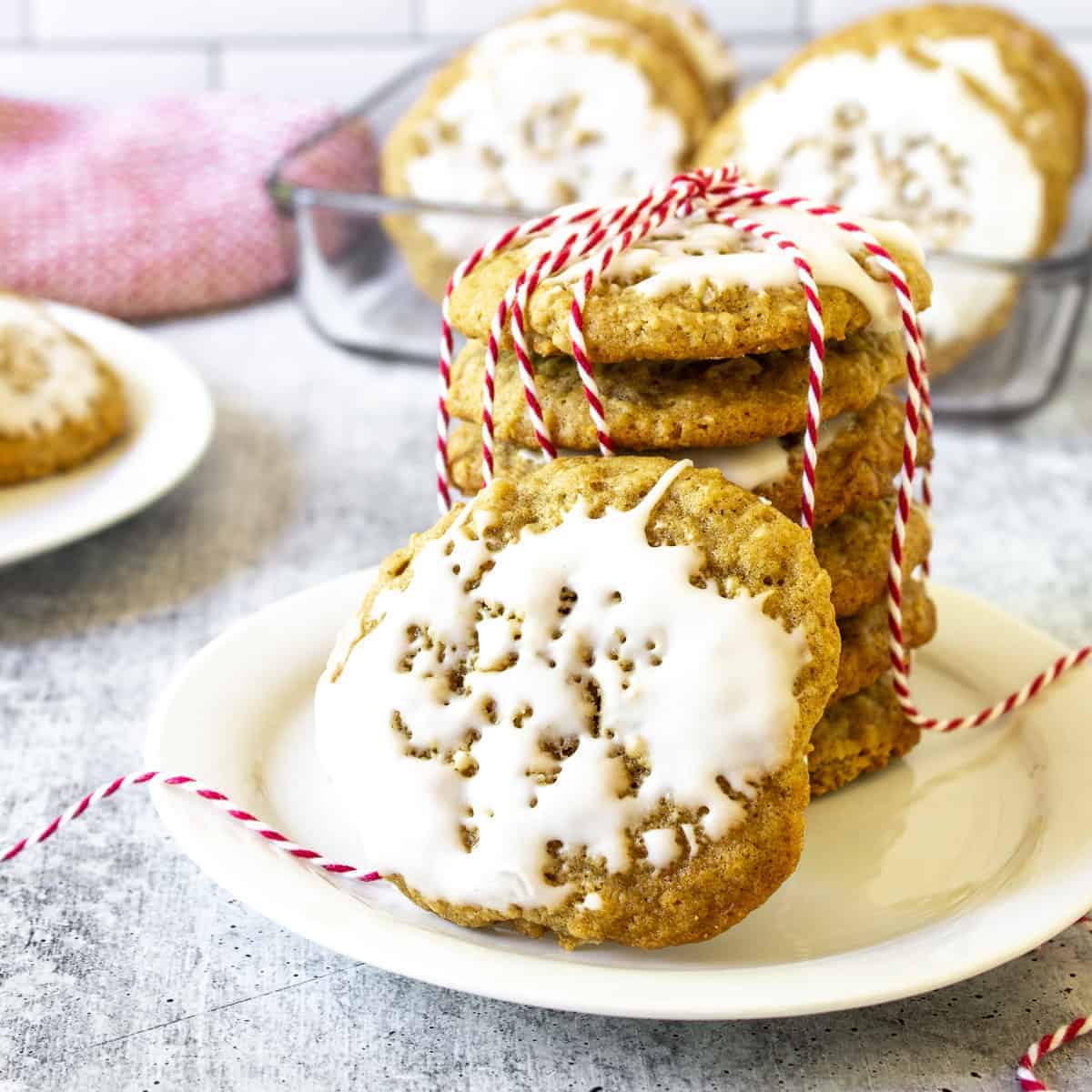 A plate with a stack of iced oatmeal cookies with red and white twine.