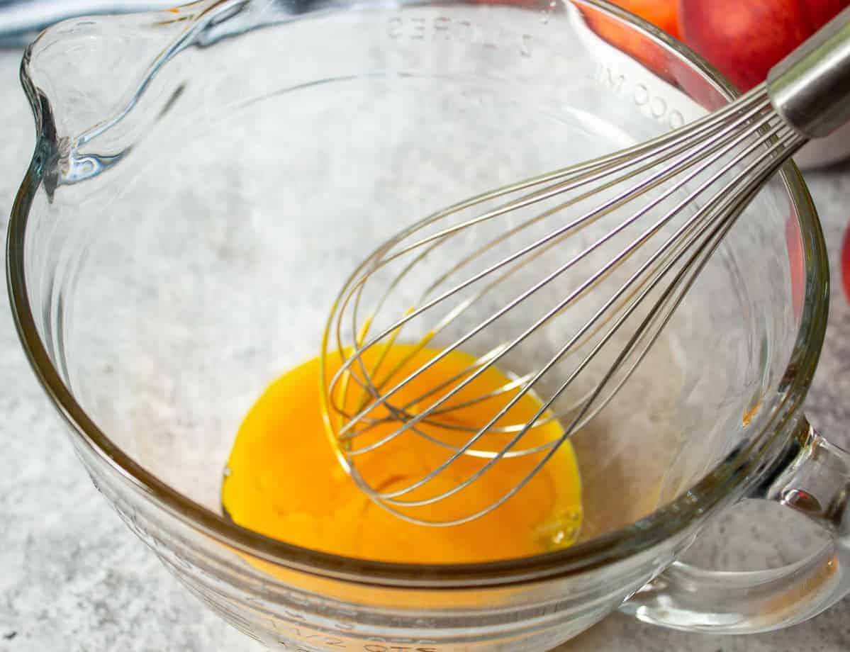 Egg yolk in a glass bowl with a wire whisk.