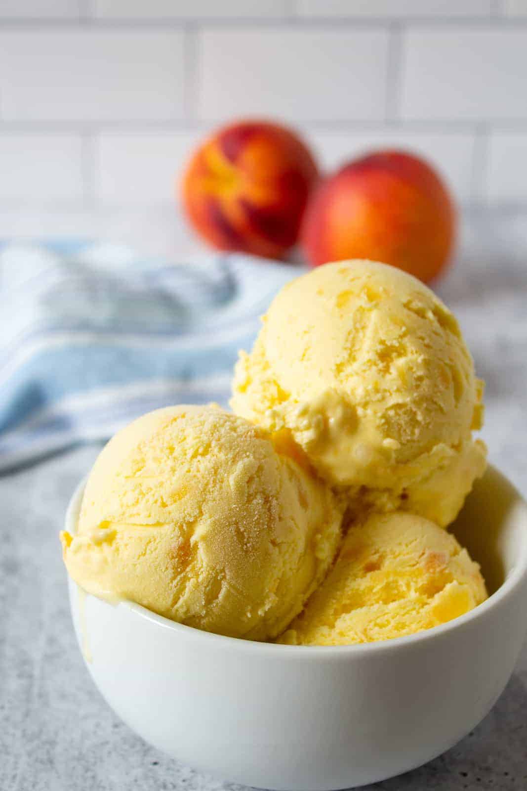 A bowl filled with scoops of ice cream with bits of peaches. 