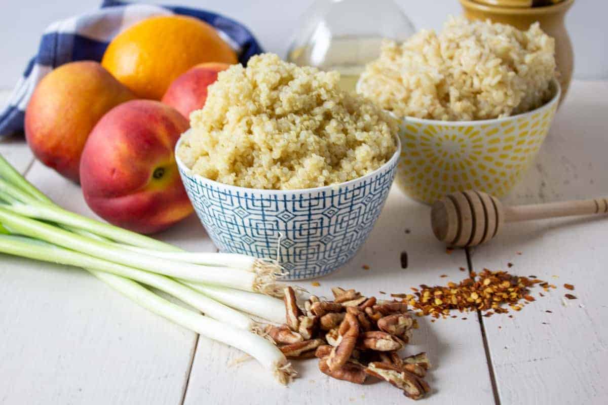 Bowls of quinoa and rice with fresh peaches and green onions next to the bowls. 