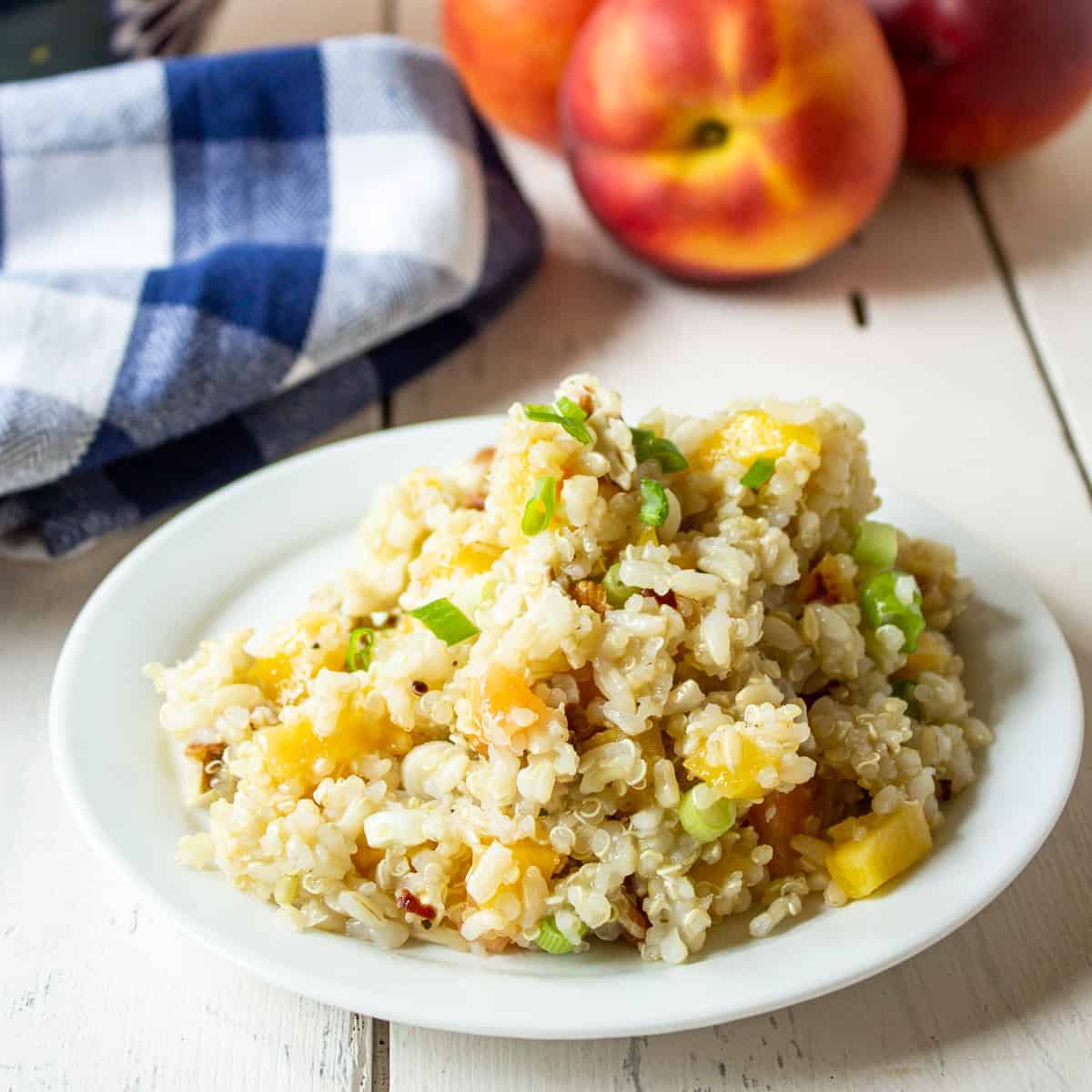 Quinoa, Rice and Peach Salad on a small white plate with fresh peaches in the background.