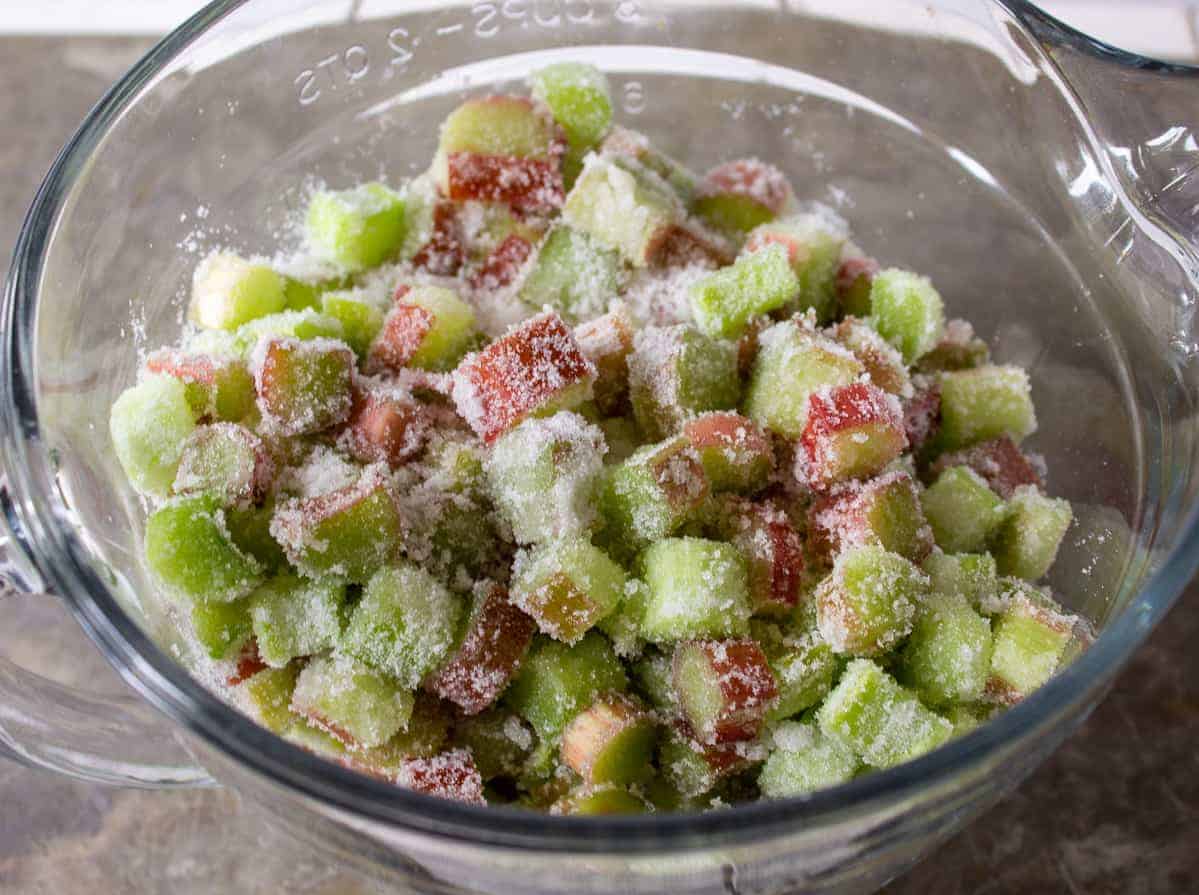 Sugar coating chopped rhubarb in a glass bowl.